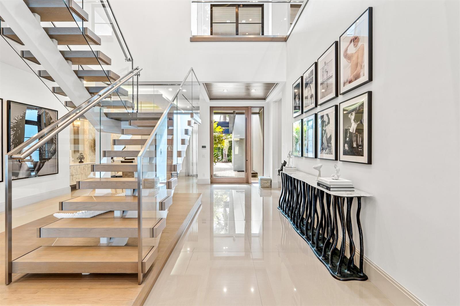 A bright entryway features a floating staircase, a console table, and framed wall art — 1040 S Ocean Boulevard, Delray Beach FL 33483, DELRAY BEACH, FL