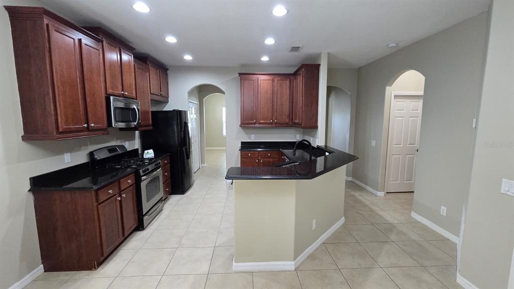 A kitchen features dark wood cabinets, black countertops, stainless steel appliances, and beige tile flooring — 314 WINTERSIDE DRIVE, APOLLO BEACH, FL