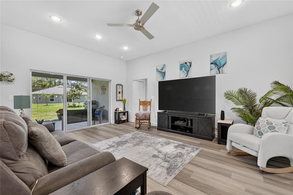 A living room features a gray sofa, a large television, a rocking chair, and sliding doors — 70 PARKWAY DRIVE, PALM COAST, FL