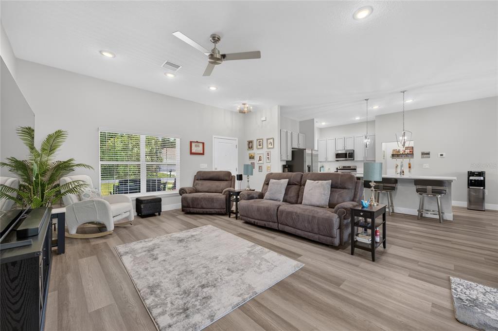 A living room with gray wood-look flooring, a brown sofa, and an open-concept kitchen — 70 PARKWAY DRIVE, PALM COAST, FL
