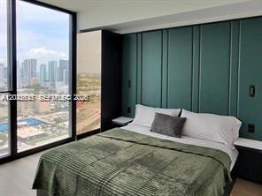 A bedroom features a green paneled accent wall, a bed, and floor-to-ceiling windows with city views — 20 NE 11th ST # 3503B, Miami FL 33132, MIAMI, FL