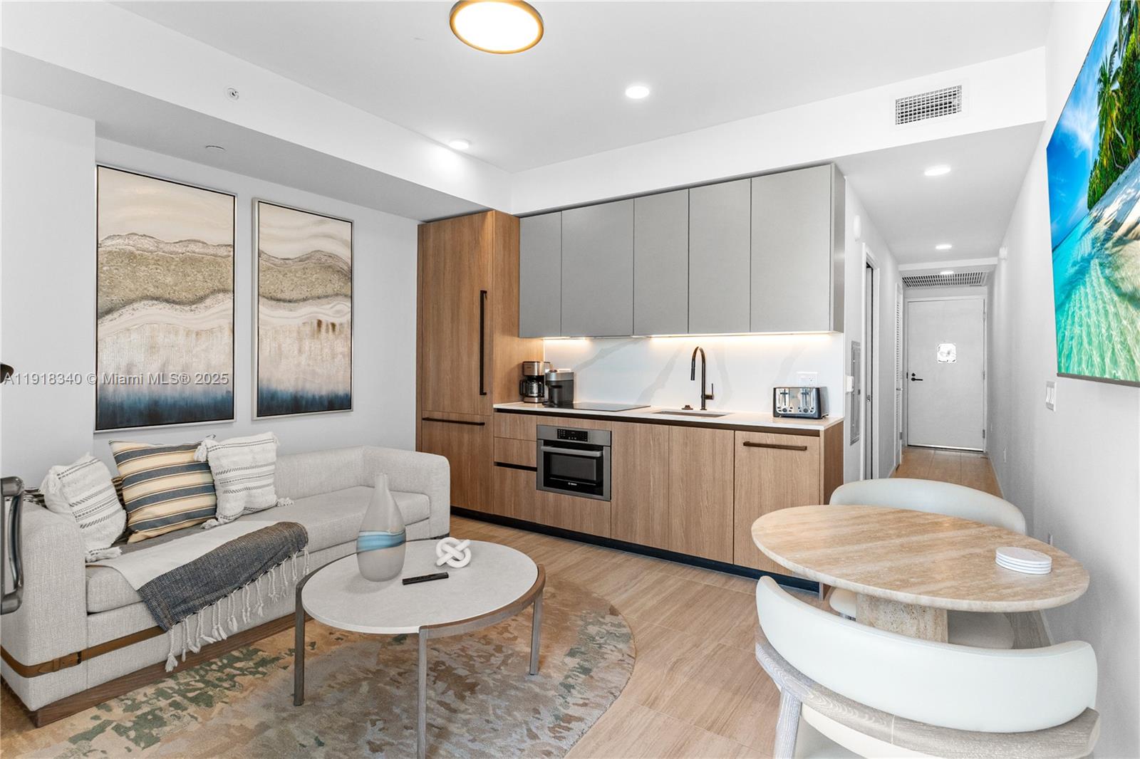 A modern studio apartment features a kitchenette with wood cabinets and a small dining area — 580 72nd # 711, Miami Beach FL 33141, MIAMI BEACH, FL
