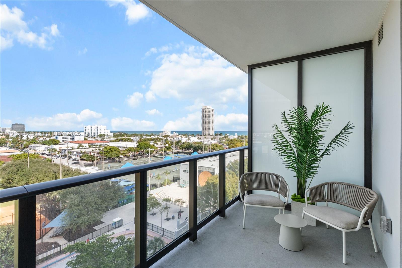 A balcony features two chairs, a small table, a potted plant, and a city view — 580 72nd # 711, Miami Beach FL 33141, MIAMI BEACH, FL