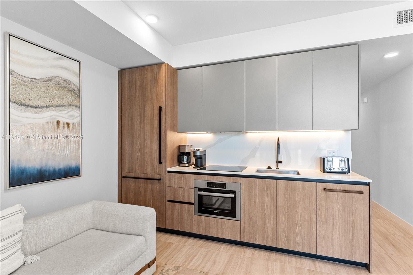 A modern kitchenette features wood-grain lower cabinets, gray upper cabinets, and integrated appliances — 580 72nd # 711, Miami Beach FL 33141, MIAMI BEACH, FL