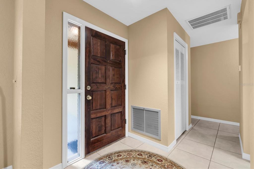 An entryway features a dark wood door, a sidelight window, and beige walls with tile flooring — 6812 RIDGE TOP DRIVE, NEW PORT RICHEY, FL