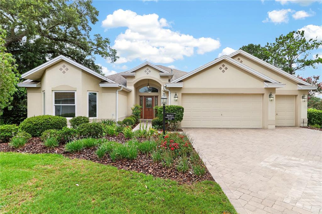 A single-story house with a beige stucco exterior, a paved driveway, and a landscaped yard — 16815 SE 85TH BELKNAP AVENUE, THE VILLAGES, FL