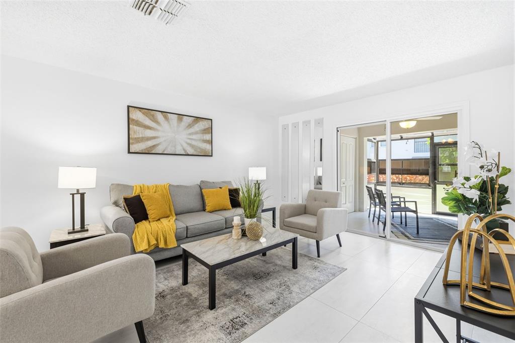 A living room with a grey sofa, two armchairs, a coffee table, and sliding glass doors — 5265 E BAY DRIVE UNIT 114, CLEARWATER, FL