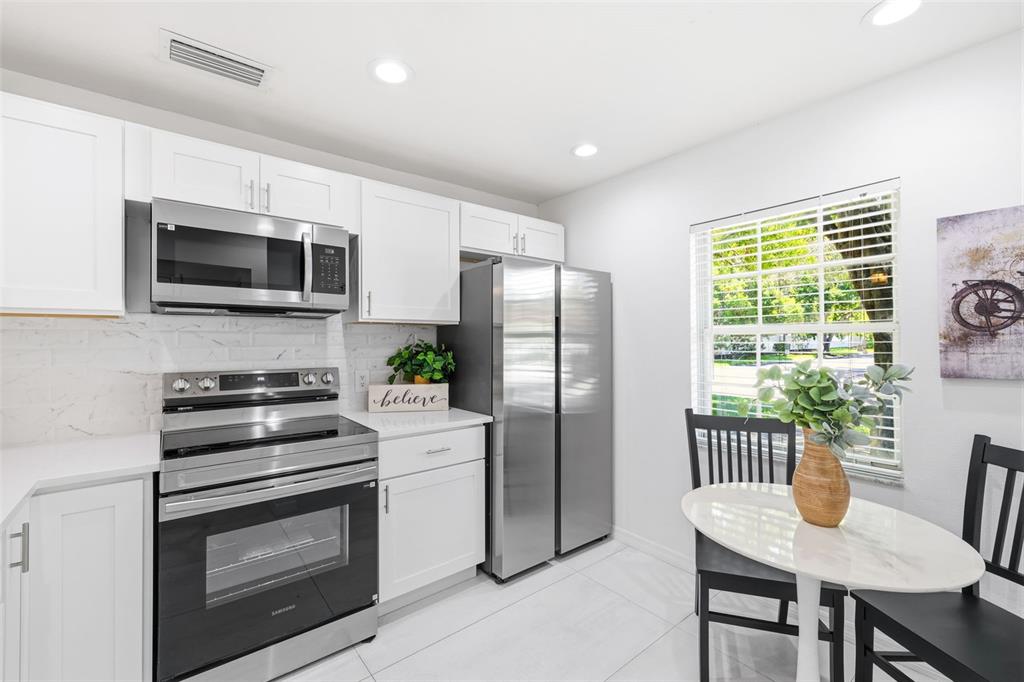 A kitchen features white cabinets, stainless steel appliances, a marble-topped table, and a window — 5265 E BAY DRIVE UNIT 114, CLEARWATER, FL