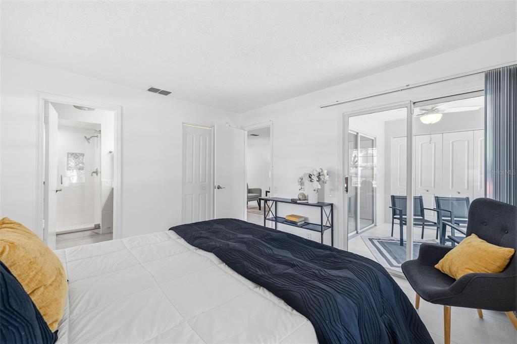 A bedroom with a white bed, a dark armchair, and a sliding door to a patio — 5265 E BAY DRIVE UNIT 114, CLEARWATER, FL