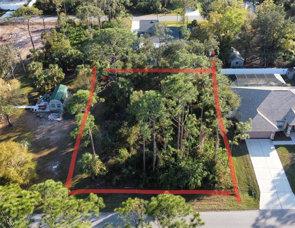An aerial view shows a vacant, tree-covered residential lot outlined in red between two houses — SYLVANIA AVENUE, NORTH PORT, FL