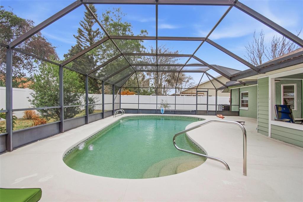 A screened-in swimming pool with a concrete deck and a white privacy fence in the background — 22 FORDHAM LANE, PALM COAST, FL