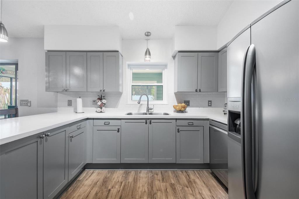 A kitchen features gray cabinets, white countertops, stainless steel appliances, and wood-look flooring — 22 FORDHAM LANE, PALM COAST, FL