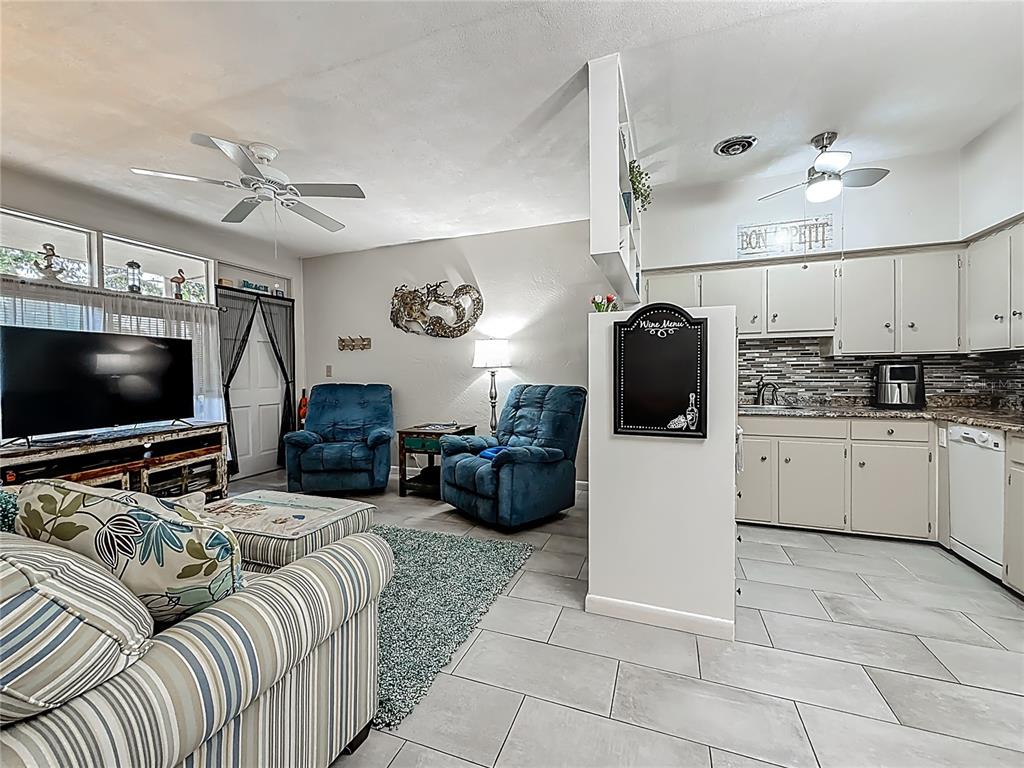 An open-concept living room and kitchen featuring tile flooring, blue recliners, and light-colored cabinetry — 4051 58TH STREET N UNIT 239C, ST PETERSBURG, FL