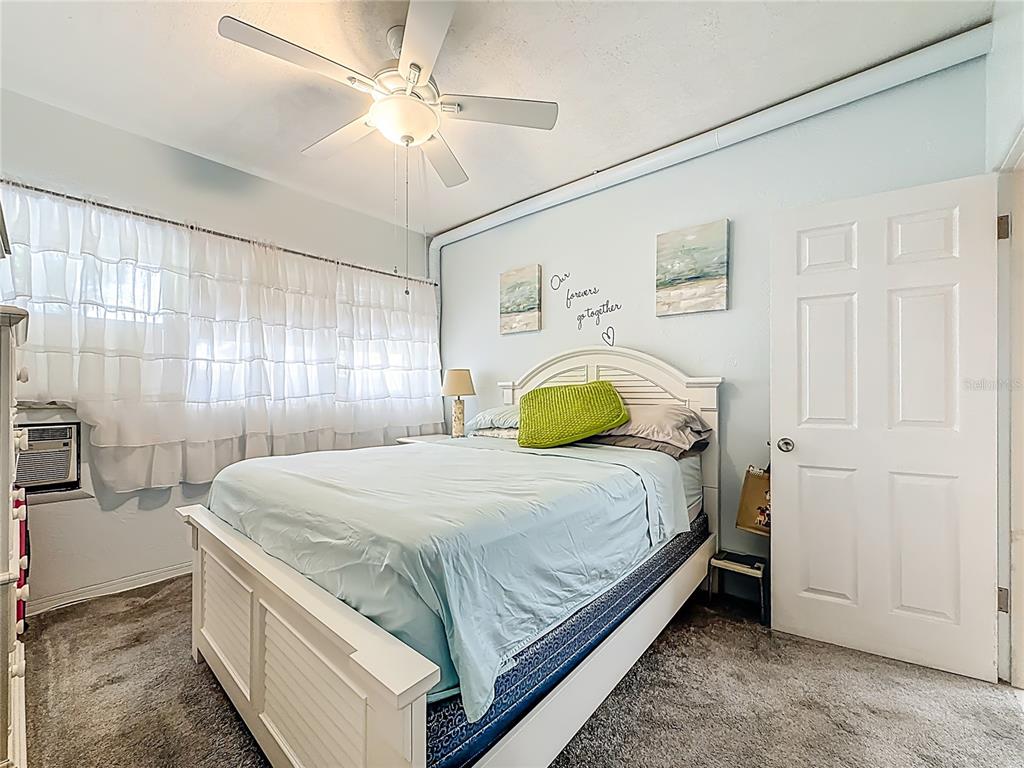A bedroom features a white bed frame, light blue bedding, a ceiling fan, and white curtains — 4051 58TH STREET N UNIT 239C, ST PETERSBURG, FL
