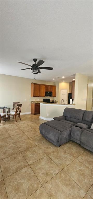 An open-concept living room and kitchen featuring tile flooring, a grey sectional, and wood cabinets — 8504 SHALLOW CREEK COURT, NEW PORT RICHEY, FL