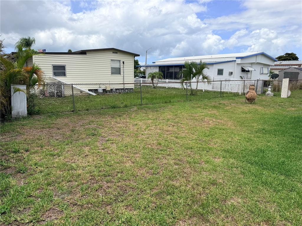 A grassy backyard features a chain-link fence separating two manufactured homes under a cloudy sky — 208 50TH AVENUE DRIVE E, BRADENTON, FL
