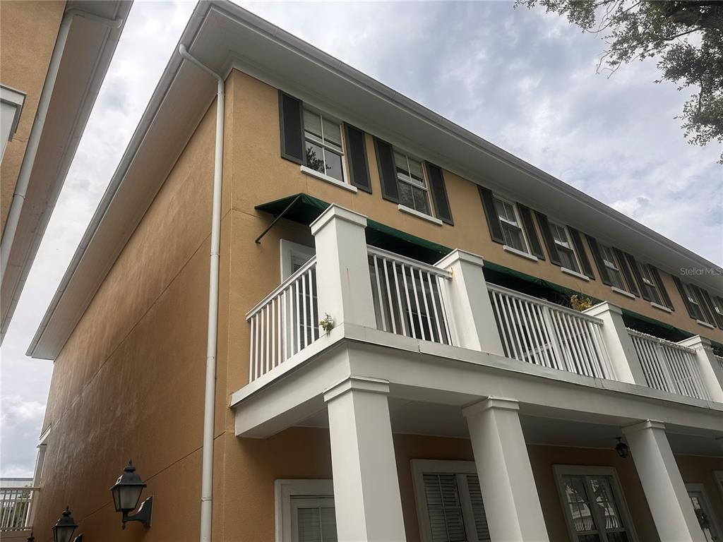 A low-angle exterior view of a tan building featuring a white balcony and columns — 709 BLOOM STREET UNIT 240, CELEBRATION, FL