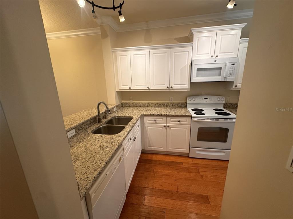 A kitchen features white cabinets, granite countertops, stainless steel appliances, and hardwood flooring — 709 BLOOM STREET UNIT 240, CELEBRATION, FL