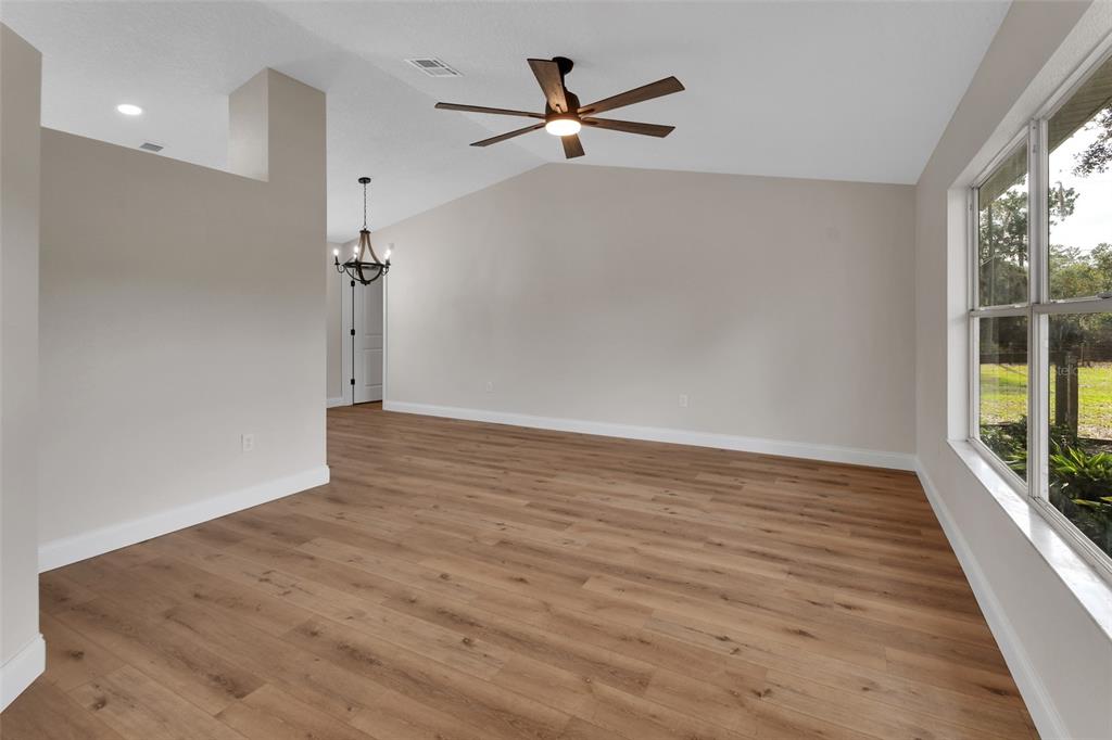 An empty room features light wood-look flooring, a vaulted ceiling with a fan, and large windows — 1251 SEMINOLE DRIVE, DE LEON SPRINGS, FL