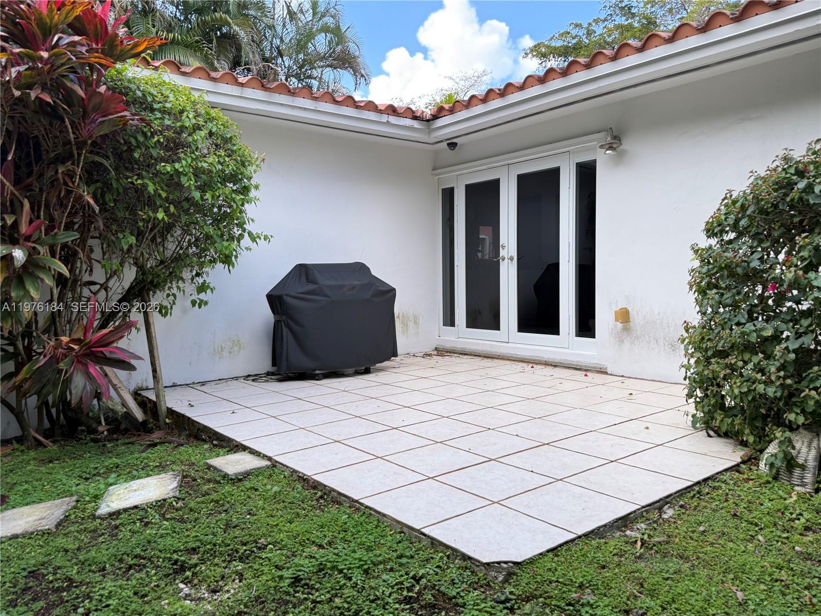 A patio with white square tiles, a covered grill, and double glass doors — 1428 Ortega Ave, Coral Gables FL 33134, CORAL GABLES, FL