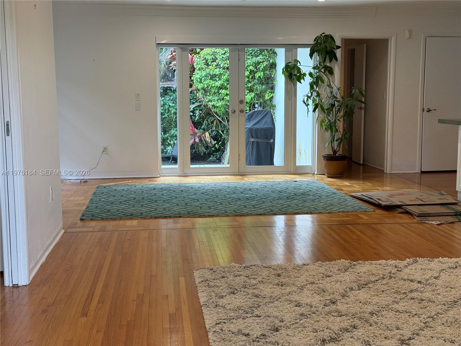 A living room features hardwood floors, a patterned rug, and glass doors opening to greenery — 1428 Ortega Ave, Coral Gables FL 33134, CORAL GABLES, FL