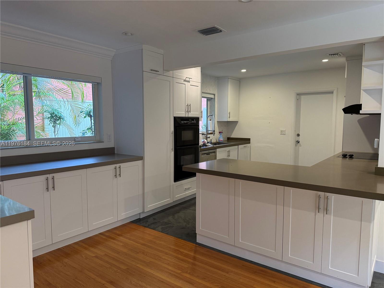 A kitchen features white cabinets, gray countertops, stainless steel appliances, and hardwood flooring — 1428 Ortega Ave, Coral Gables FL 33134, CORAL GABLES, FL