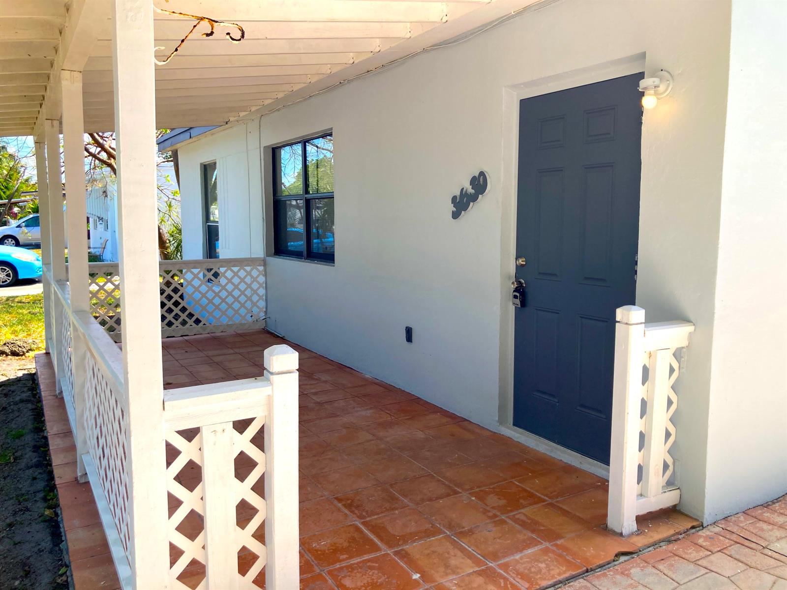 A covered porch with terracotta tile flooring, white lattice railings, and a dark blue front door — 3630 SW 46th Avenue, West Park FL 33023, WEST PARK, FL