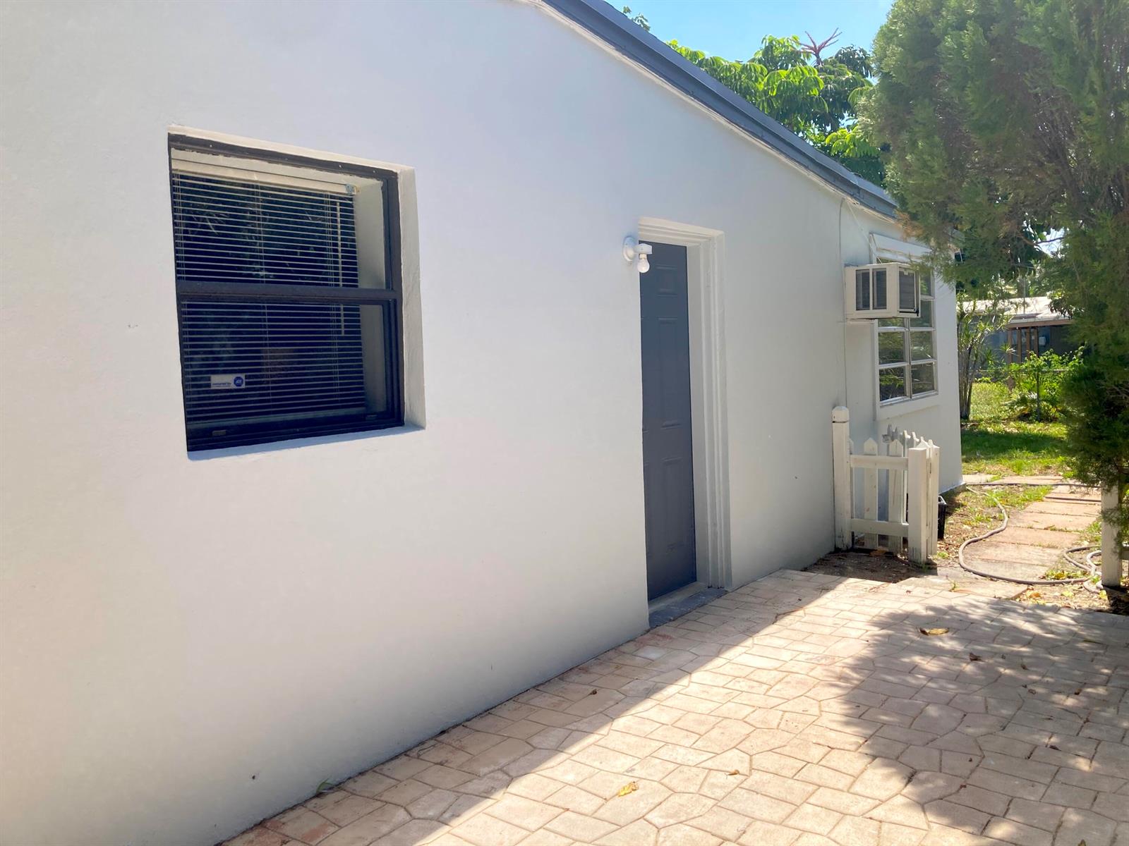 A white exterior wall features a window, a dark door, and a small patio area — 3630 SW 46th Avenue, West Park FL 33023, WEST PARK, FL
