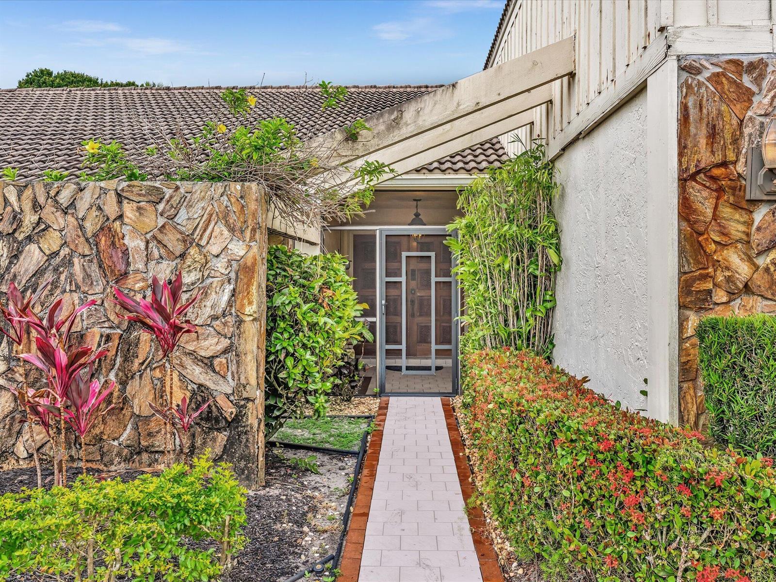 A stone-walled walkway leads to a front entrance with a glass storm door — 5302 Piping Rock Drive, Boynton Beach FL 33437, BOYNTON BEACH, FL