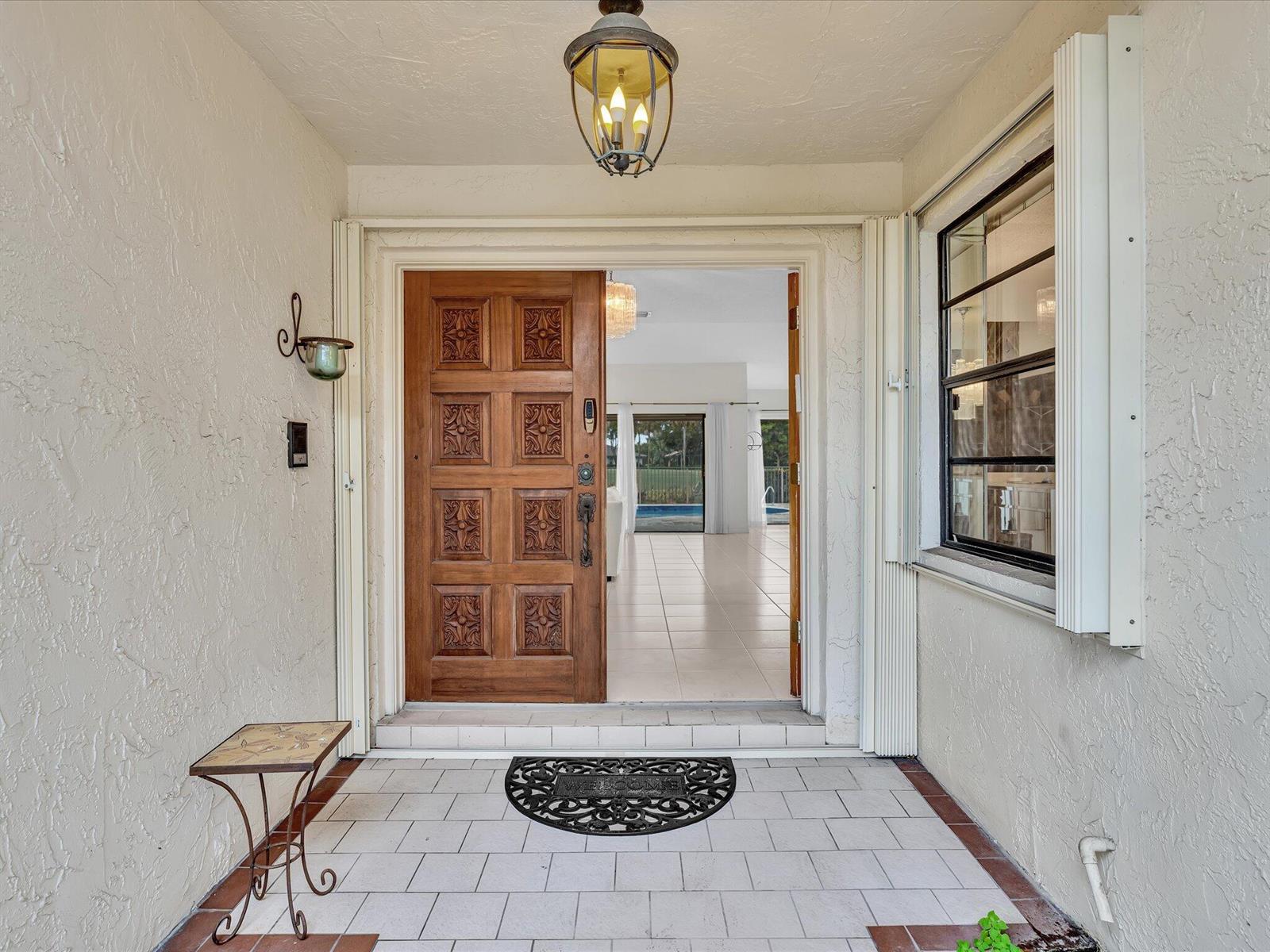 A covered entryway features a carved wooden door, a tiled floor, and a hanging lantern — 5302 Piping Rock Drive, Boynton Beach FL 33437, BOYNTON BEACH, FL
