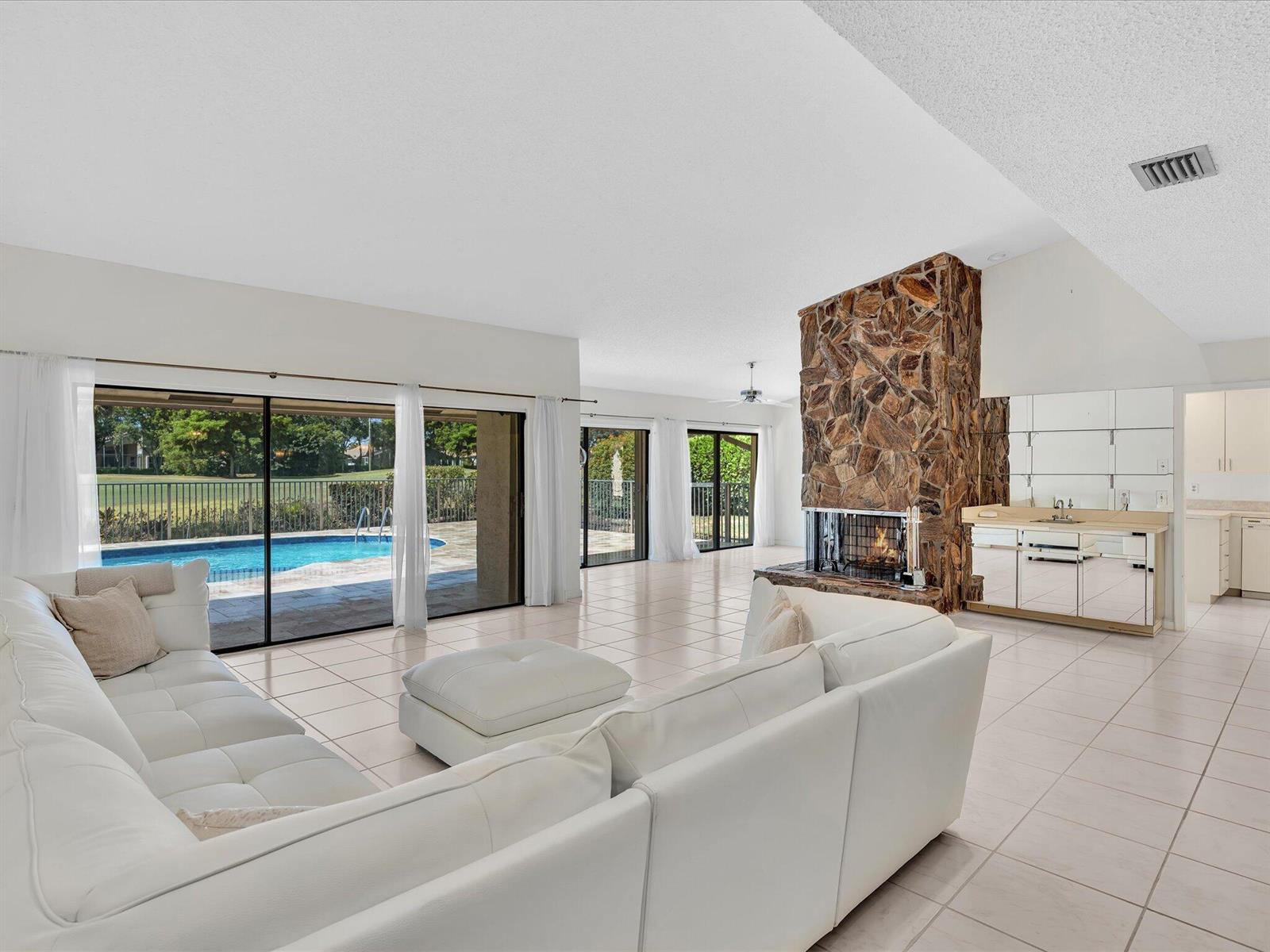 A living room features a stone fireplace, white tile floors, and sliding doors to a pool — 5302 Piping Rock Drive, Boynton Beach FL 33437, BOYNTON BEACH, FL