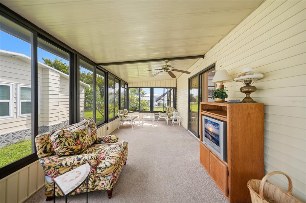 A sunroom features carpeted floors, a ceiling fan, a floral armchair, and a television console — 16209 ASHEBORO COURT, FORT MYERS, FL