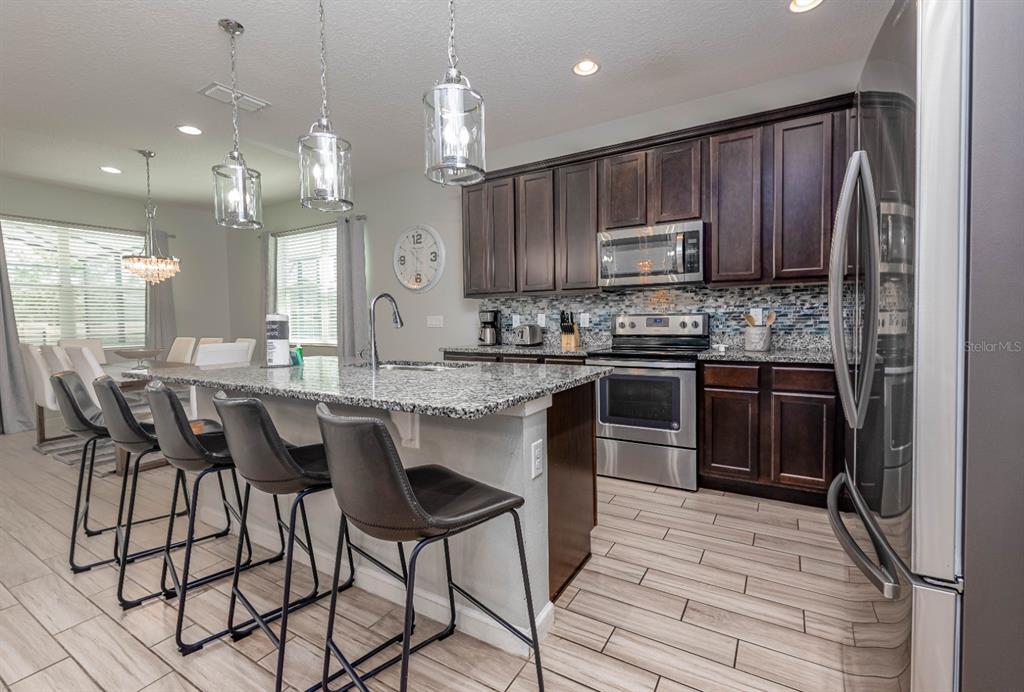 A kitchen features dark wood cabinets, granite countertops, stainless steel appliances, and a breakfast bar — 2661 CALISTOGA, KISSIMMEE, FL