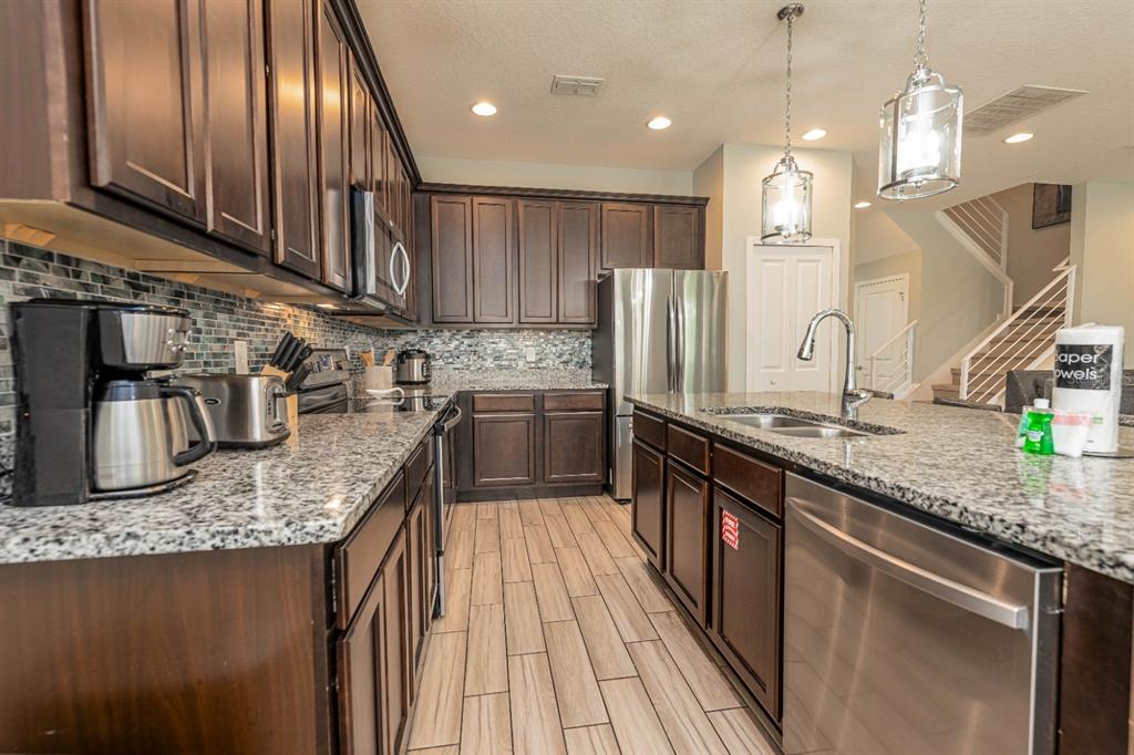 A kitchen features dark wood cabinets, granite countertops, a stainless steel refrigerator, and tile flooring — 2661 CALISTOGA, KISSIMMEE, FL