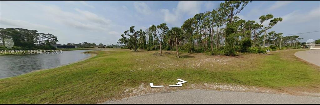 A vacant, grassy residential lot sits adjacent to a canal with scattered trees and shrubs — 13 YARDARM DRIVE, PLACIDA, FL