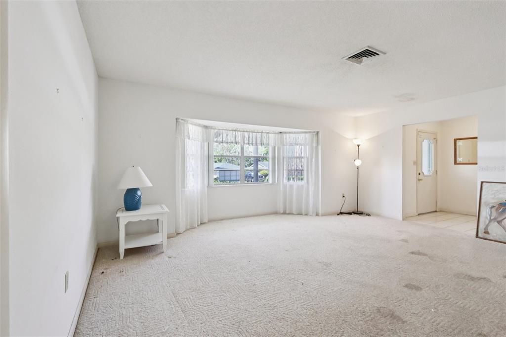 A living room with beige wall-to-wall carpeting, white walls, and a large bay window — 12 SUN AIR BOULEVARD E, HAINES CITY, FL