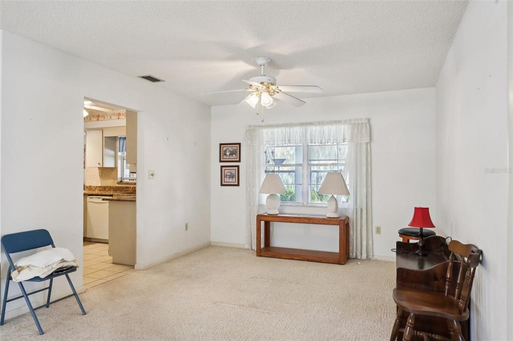A living room with beige carpet, a ceiling fan, and a view into the kitchen — 12 SUN AIR BOULEVARD E, HAINES CITY, FL