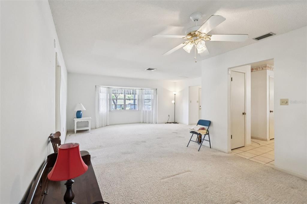 A spacious, white-walled living room features beige carpeting, a ceiling fan, and a bay window — 12 SUN AIR BOULEVARD E, HAINES CITY, FL