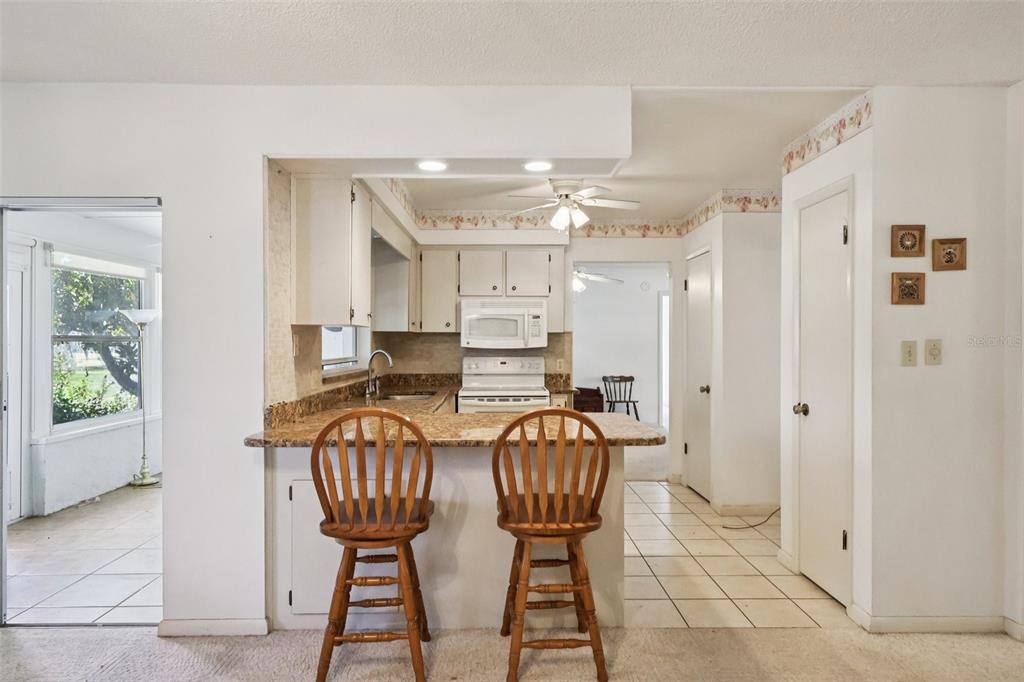 A kitchen with a breakfast bar, wooden stools, white cabinets, and tiled flooring — 12 SUN AIR BOULEVARD E, HAINES CITY, FL