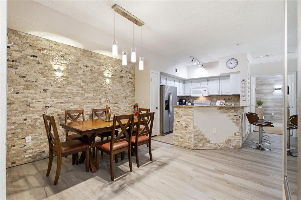 A dining area with a stone accent wall, wooden table, and an adjacent open kitchen — 13037 MULBERRY PARK DRIVE UNIT 518, ORLANDO, FL