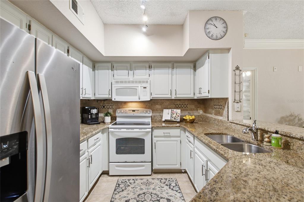 A kitchen features white cabinets, granite countertops, stainless steel appliances, and a tile floor — 13037 MULBERRY PARK DRIVE UNIT 518, ORLANDO, FL