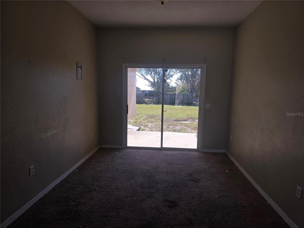 An empty room with beige walls, brown carpeting, and a sliding glass door to a yard — 4049 BYRDS CROSSING DRIVE, LAKELAND, FL