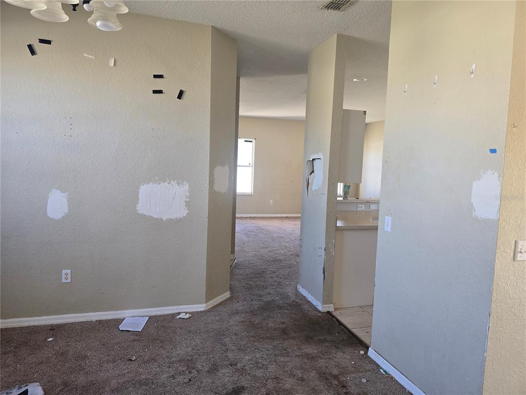 An interior view shows a carpeted room with beige walls, patches of spackle, and wall damage — 4049 BYRDS CROSSING DRIVE, LAKELAND, FL