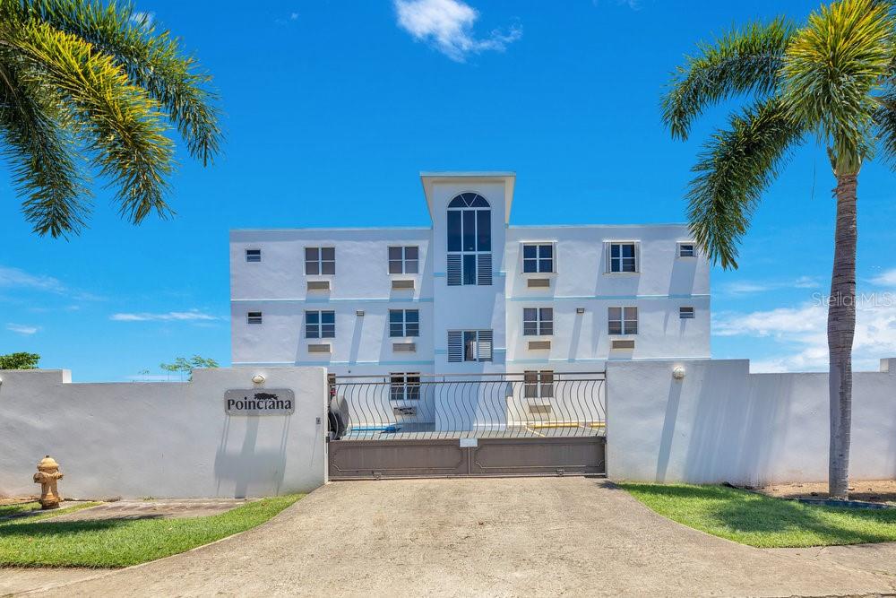 A white three-story apartment building stands behind a gated entrance with palm trees — km 4.1, PR-413 Rincon 006 KM 4.1, PR- 413 RINCON 00677 UNIT A7, RINCON, PR