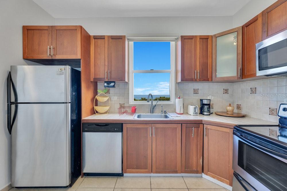 A kitchen with wood cabinets, stainless steel appliances, tile countertops, and a window overlooking water — km 4.1, PR-413 Rincon 006 KM 4.1, PR- 413 RINCON 00677 UNIT A7, RINCON, PR