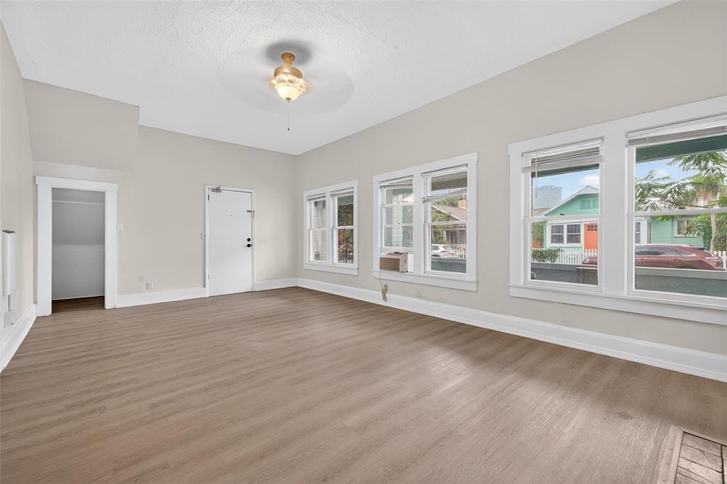 An empty living room features light wood-look flooring, white walls, and several windows — 633 7TH AVENUE N, ST PETERSBURG, FL