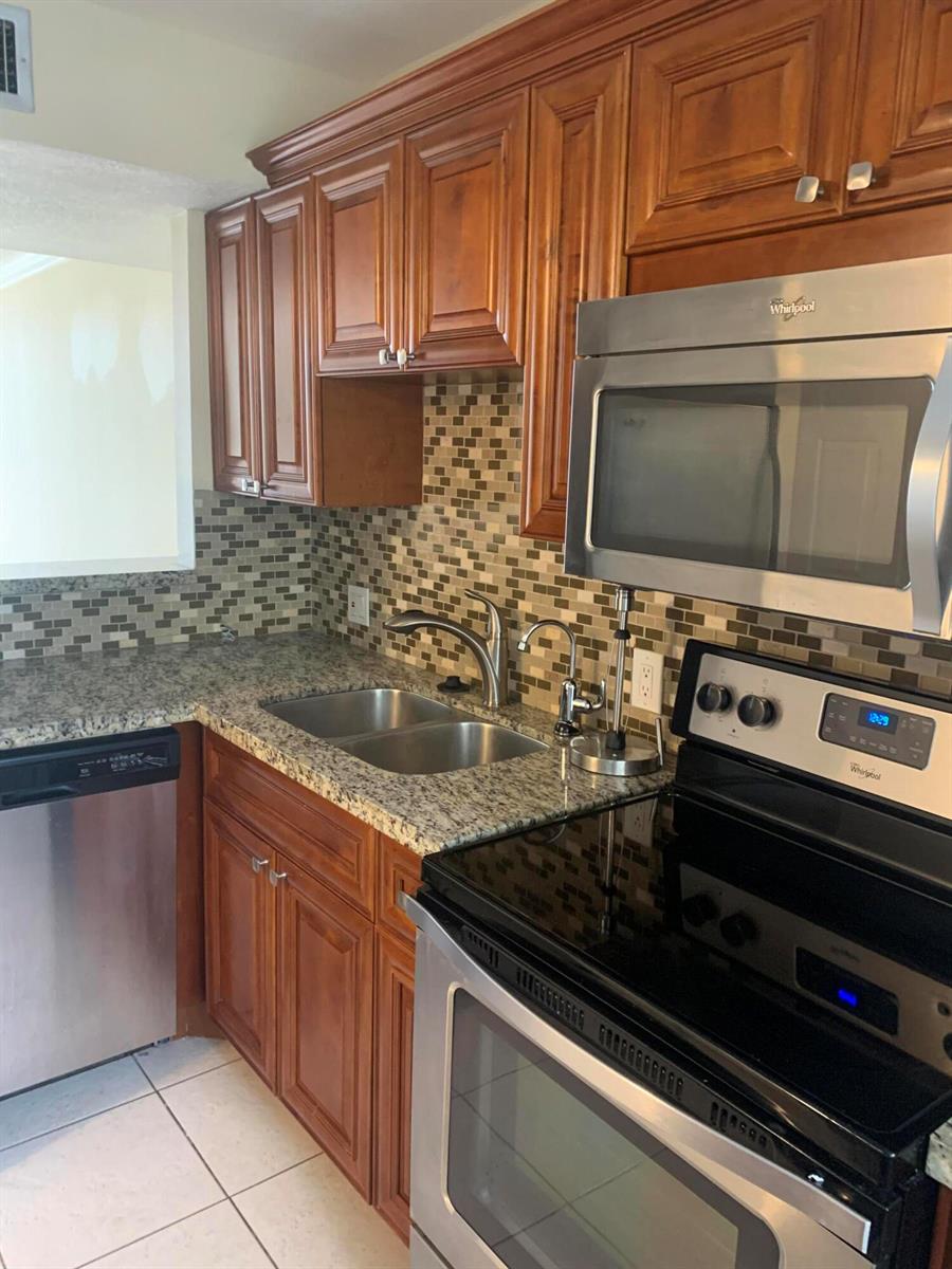 A kitchen features wood cabinets, granite countertops, a mosaic tile backsplash, and stainless steel appliances — 4236 Deste # 108, Lake Worth FL 33467, LAKE WORTH, FL