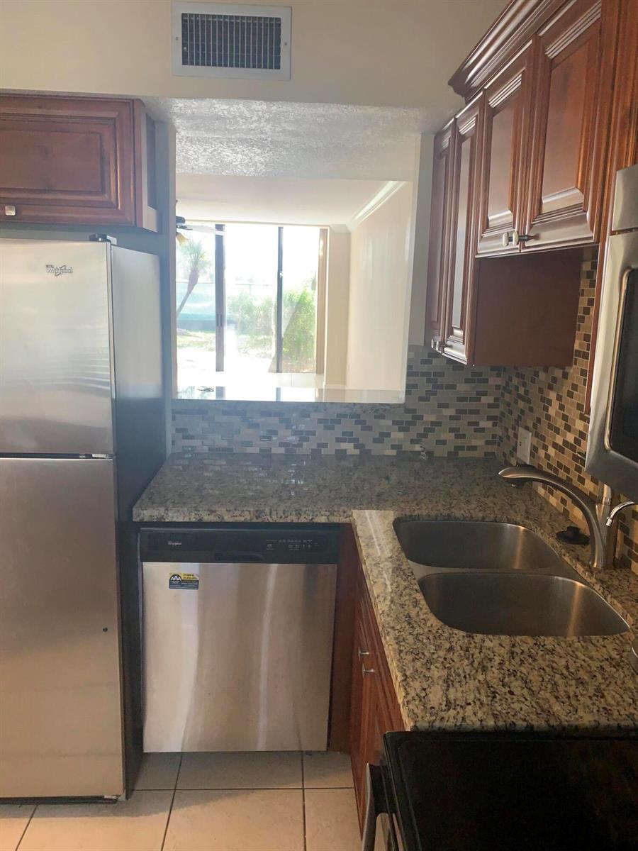 A kitchen features stainless steel appliances, granite countertops, wood cabinets, and a tiled backsplash — 4236 Deste # 108, Lake Worth FL 33467, LAKE WORTH, FL