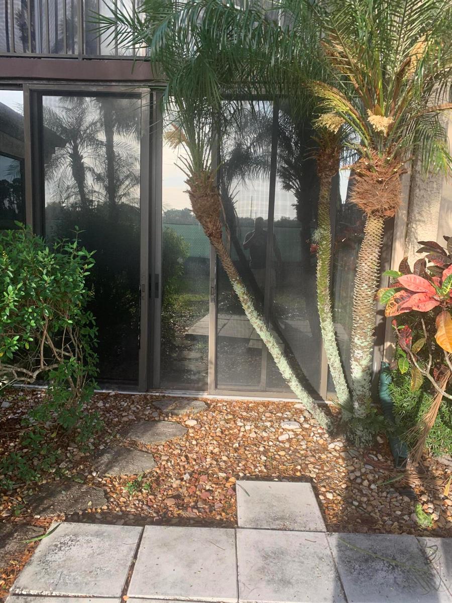 A sliding glass door opens to a patio area with palm trees and stone pavers — 4236 Deste # 108, Lake Worth FL 33467, LAKE WORTH, FL