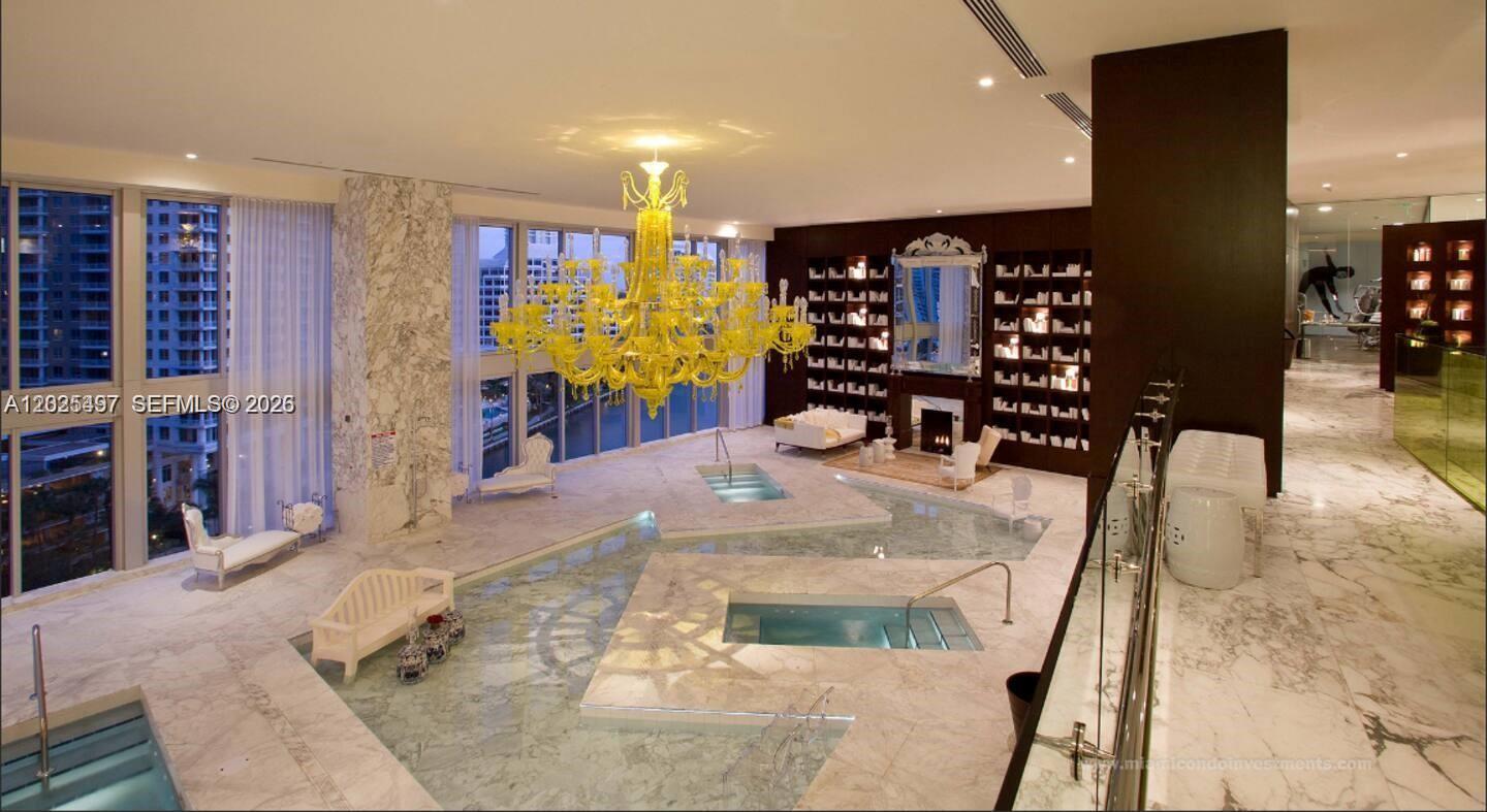 A luxurious indoor pool room features marble flooring, a large yellow chandelier, and floor-to-ceiling windows — 485 Brickell Ave # 2006, Miami FL 33131, MIAMI, FL
